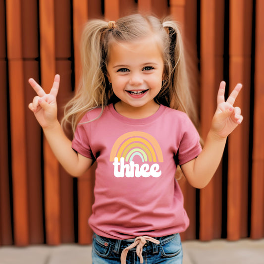 Close-up of retro rainbow birthday graphic on a girls purple 3rd birthday tee by Olive Loves Apple