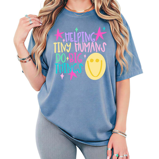 Flat lay of Helping Tiny Humans Do Big Things kindergarten teacher tee showing full design detail and soft garment-dyed fabric