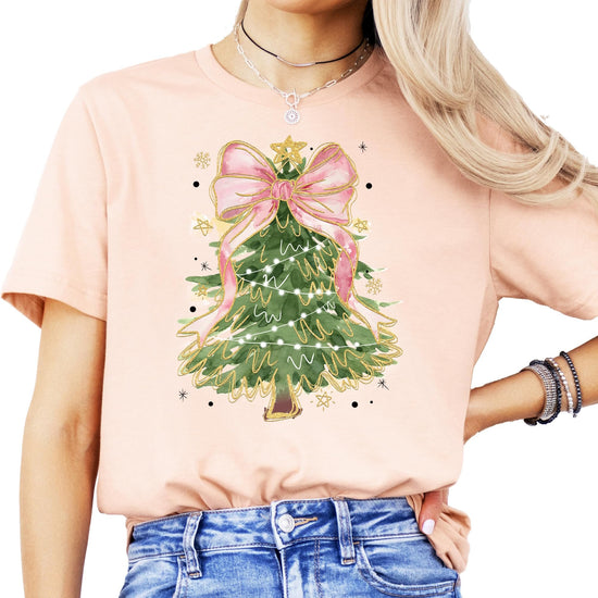 Model wearing festive Christmas tree pink bow tee in peach, casual holiday style