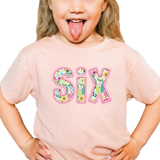 Girls wearing peach sixth birthday shirt with colorful floral number six graphic print