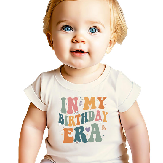 Front view of girls birthday graphic t-shirt with 'In My Birthday Era' wavy text print in peach