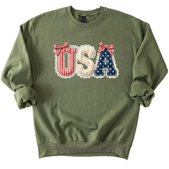 White crewneck sweatshirt with USA text in red stripes, cream cable-knit, and navy stars with decorative bows